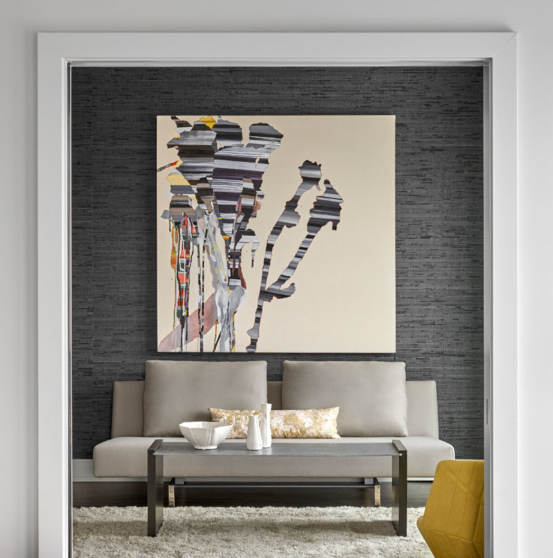 This small lounge area is highlighted by the dark grey accent wall, the large art piece, and a colorful yellow armchair. #InteriorDesign #ModernInterior