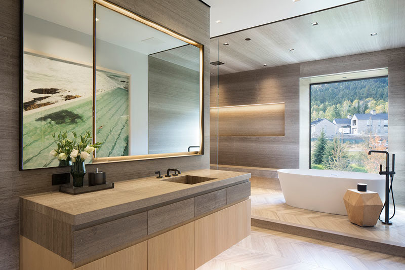 Bathroom Ideas - In this modern master bathroom, hidden lighting creates a soft glow, while the freestanding bathtub has been raised up on a platform and positioned beneath the window. #BathroomIdeas #ModernBathroom #MasterBathroom