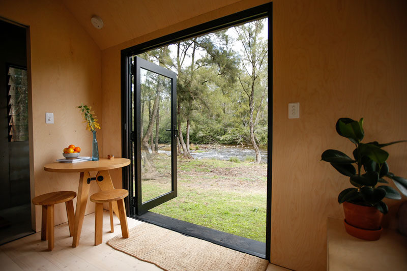 The black-framed glass french doors of this tiny house can be opened to help make the interior feel larger. Just inside the doors is a small corner dedicated to a round table and a pair of stools. #TinyHouse #TinyHome #TinyCabin #Doors