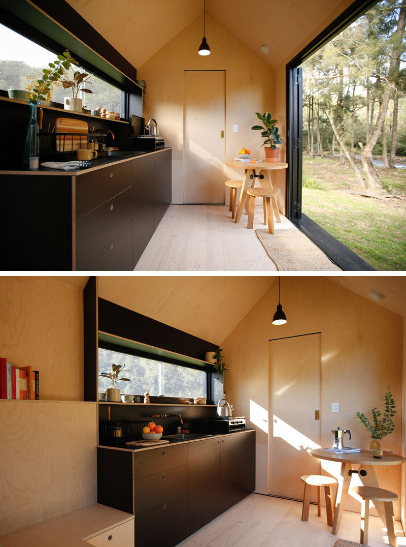 This modern tiny cabin has a cathedral ceiling adding to the sense of openness, while the dark kitchen cabinets and shelving are located around a long horizontal window. #TinyHouse #TinyHome #TinyCabin #BlackKitchen