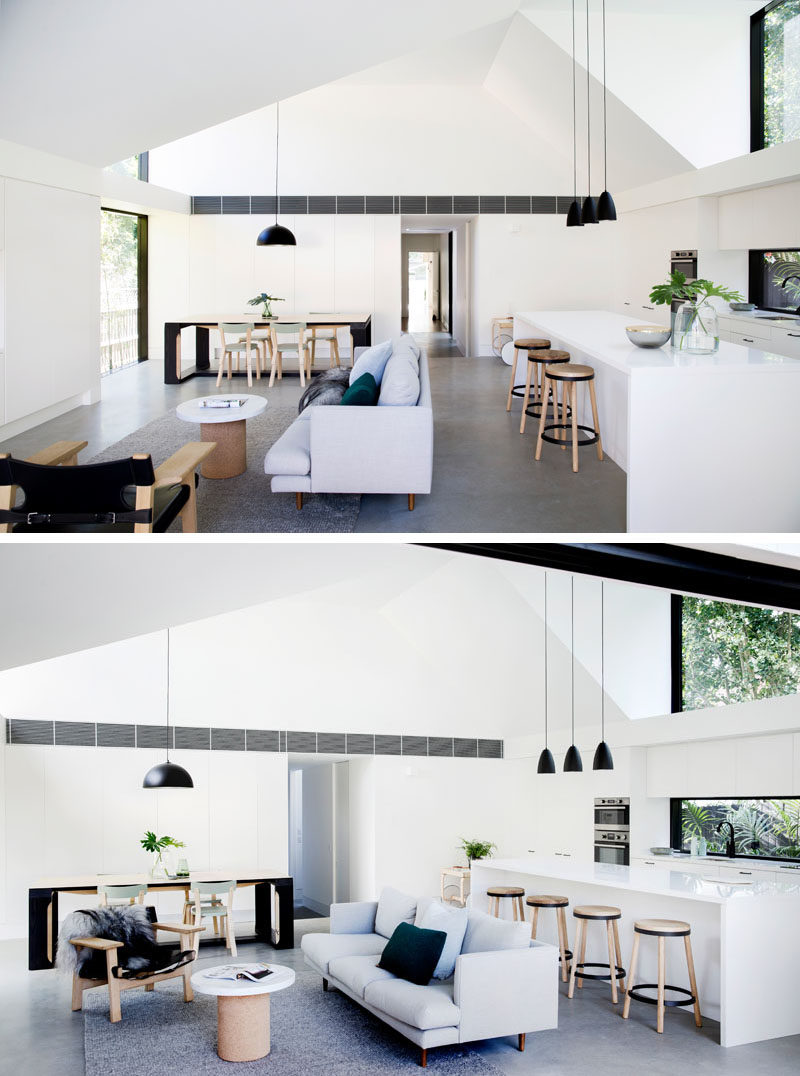 The monochrome aesthetic of this open plan living room, dining room, and kitchen, has been softened by timber furniture, which adds warmth to the large space.  #InteriorDesign #ModernInterior #WhiteInterior #BlackPendantLights