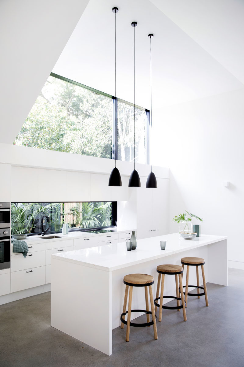 Kitchen Ideas - In this modern kitchen, three black pendant lights above the island draw the eye upwards to highlight the double-height ceiling, while the white cabinets help the kitchen blend into the white walls. #KitchenDesign #KitchenIdeas #WhiteKitchen