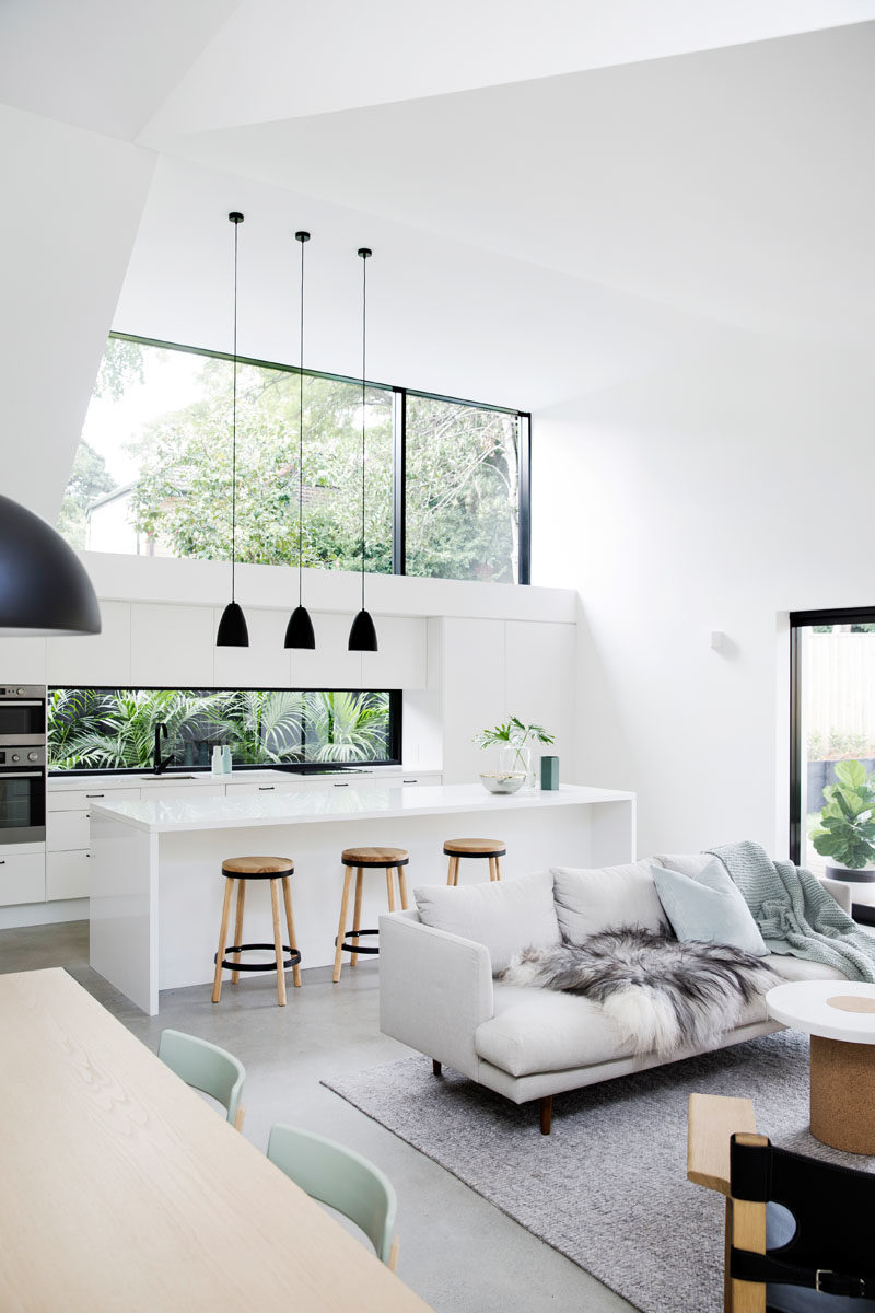 Kitchen Ideas - In this modern kitchen, three black pendant lights above the island draw the eye upwards to highlight the double-height ceiling, while the white cabinets help the kitchen blend into the white walls. #KitchenDesign #KitchenIdeas #WhiteKitchen