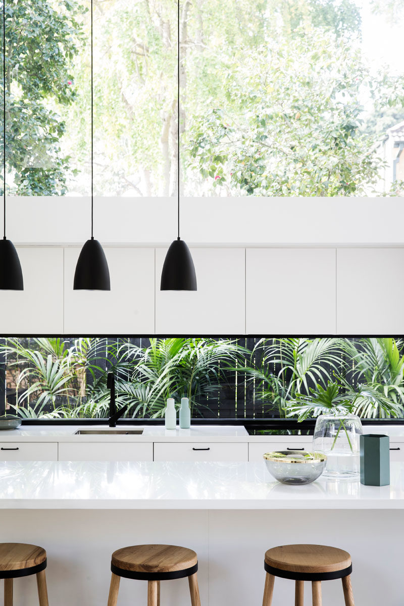 Kitchen Ideas - In this modern kitchen, three black pendant lights above the island draw the eye upwards to highlight the double-height ceiling, while the white cabinets help the kitchen blend into the white walls. #KitchenDesign #KitchenIdeas #WhiteKitchen