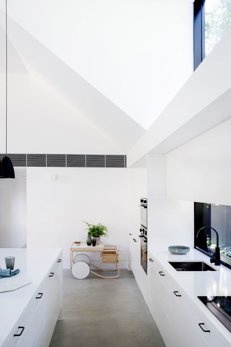 Kitchen Ideas - In this modern kitchen, three black pendant lights above the island draw the eye upwards to highlight the double-height ceiling, while the white cabinets help the kitchen blend into the white walls. #KitchenDesign #KitchenIdeas #WhiteKitchen