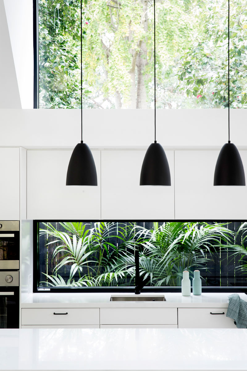 Kitchen Ideas - In this modern kitchen, three black pendant lights above the island draw the eye upwards to highlight the double-height ceiling, while the white cabinets help the kitchen blend into the white walls. #KitchenDesign #KitchenIdeas #WhiteKitchen