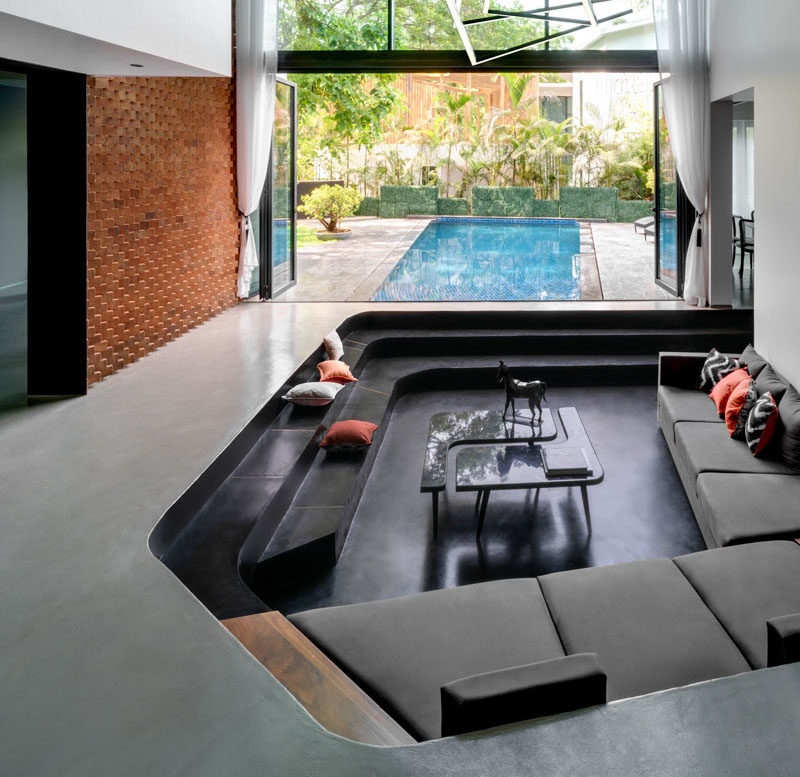 Sunken Living Room Ideas - This modern house features a curved sunken living room that has amphitheater like seating made from polished concrete, and sits beside double-height doors that fold open to connect the living room with the pool and patio outside. #SunkenLivingRoom #LivingRoomIdeas #BuiltInSeating