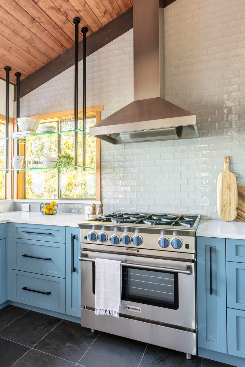 Kitchen Ideas - On each side of the stove, there's a spice/utensil pullout, keeping everything in arms reach when cooking, while a custom designed suspended shelf system allows the homeowners to display beautiful dishware and still keep their view.  #KitchenIdeas #BlueKitchen #BlueCabinets #Stove #KitchenDesign