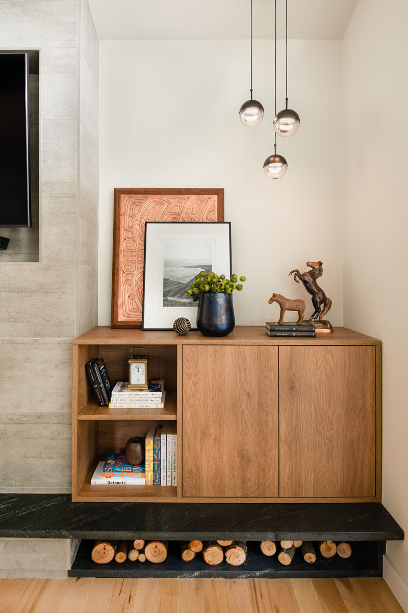 Living Room Ideas - This modern living room has light walls and wood flooring, while the fireplace surround has a recessed area for the television to be mounted in. Beside the fireplace is a custom-designed wood cabinet, and room for firewood storage. #LivingRoomIdeas #ModernLivingRoom #FirewoodStorage #FireplaceIdeas #ModernFireplace