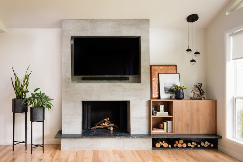 Living Room Ideas - This modern living room has light walls and wood flooring, while the fireplace surround has a recessed area for the television to be mounted in. Beside the fireplace is a custom-designed wood cabinet, and room for firewood storage. #LivingRoomIdeas #ModernLivingRoom #FirewoodStorage #FireplaceIdeas #ModernFireplace