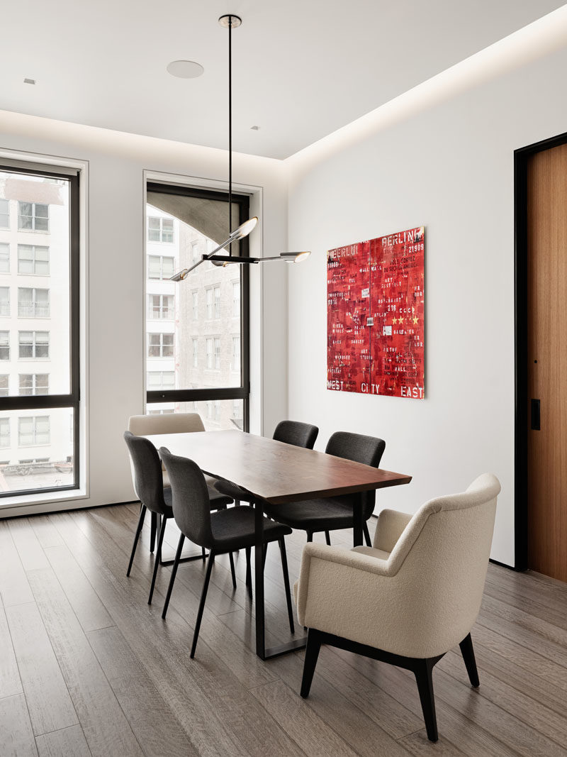 Dining Room Ideas - In this modern dining room, a minimalist pendant light hangs above the dining table, while red artwork adds a pop of color to the open interior. #DiningRoomIdeas #InteriorDesign #ModernDiningRoom