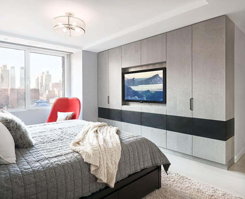 Bedroom Ideas - In this modern master bedroom, the television has been set back into the cabinets, and a blackened steel inlay provides contrast to the grey-washed birch veneer millwork. #ModernBedroom #CabinetIdeas #BedroomIdeas #Wardrobe #Closet