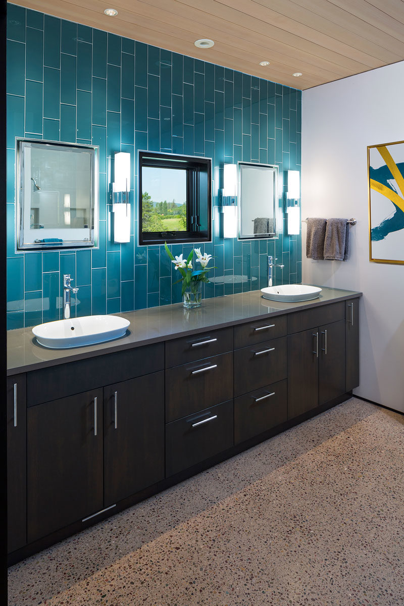 Bathroom Ideas - In this modern bathroom, blue tiles laid vertically draw attention to the height of the room. A wall-to-wall dark wood vanity provides plenty of space for two, while the mirrors are positioned on either side of the mirror. #BathroomIdeas #ModernBathroom #BlueTiles #WoodCeiling