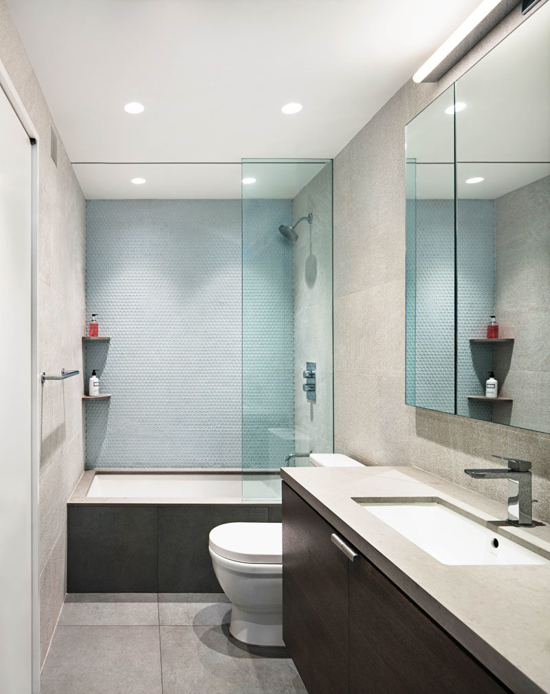 Bathroom Ideas - In this modern bathroom, light blue tiles have been used to create a soft accent wall in the bath/shower, while a dark wood vanity is topped with a grey counter. #BathroomIdeas #ModernBathroom #VanityIdeas #TileIdeas