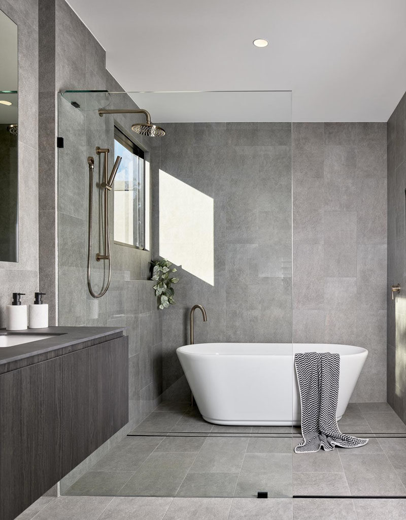 Bathroom Ideas - In this modern bathroom, grey tiles cover the walls, while a seamless glass partition separates the shower and bathtub from the rest of the room. #BathroomIdeas #BathroomDesign #GreyBathroom