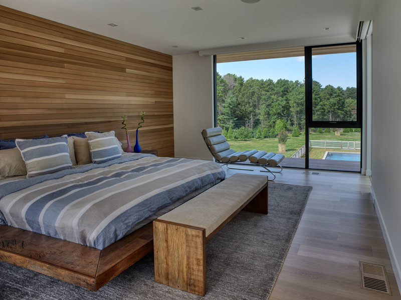 Bedroom Ideas - This modern bedroom has a wood accent wall that complements the wood found throughout the house, and the bed frame. A large window provides a view of the yard and the trees in the distance. #BedroomIdeas #MOdernBedroom #WoodAccentWall