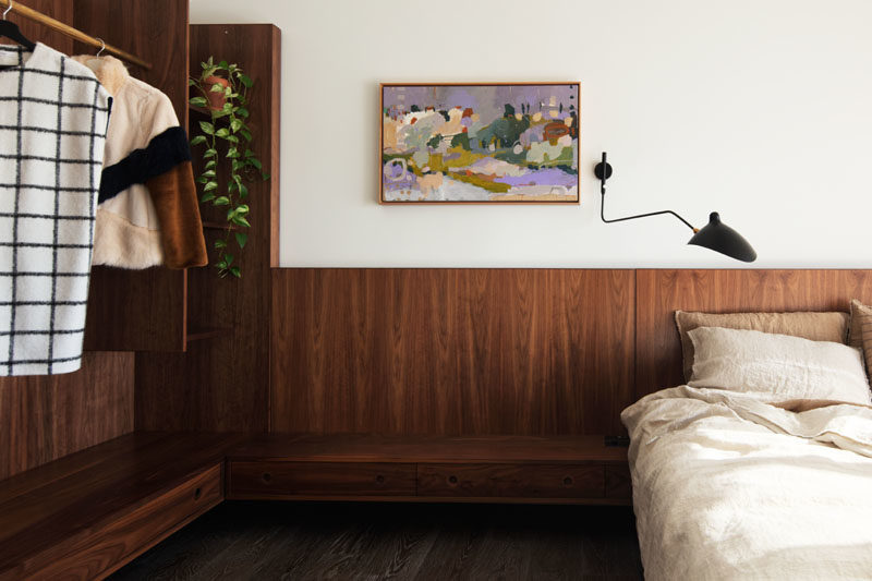 Bedroom Ideas - This modern bedroom features dark wood that has been used to create a headboard that travels along the wall to become an open closet. #BedroomDesign #BedroomIdeas #ModernBedroom #OpenCloset #WoodHeadboard