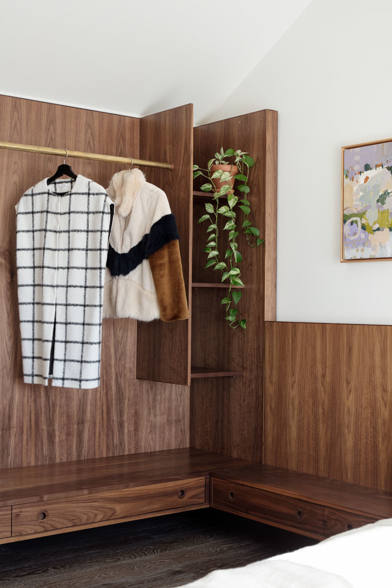 Bedroom Ideas - This modern bedroom features dark wood that has been used to create a headboard that travels along the wall to become an open closet. #BedroomDesign #BedroomIdeas #ModernBedroom #OpenCloset #WoodHeadboard