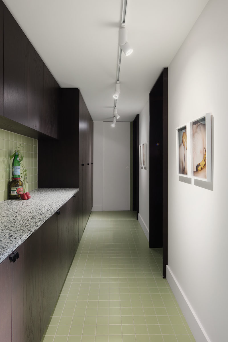 Pantry Ideas - A door in the kitchen leads to a butlers pantry that features the same dark cabinets and pastel green tiles, keeping a cohesive appearance. #ButlersPantry #Pantry #GreenTiles #DarkCabinets