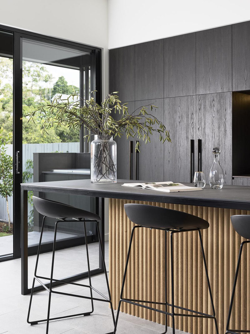 Kitchen Ideas - In this modern kitchen, minimalist dark cabinets line the wall, and an island with room for bar seating, features a wood accent. #KitchenIdeas #DarkKitchen #ModernKitchen #KitchenDesign