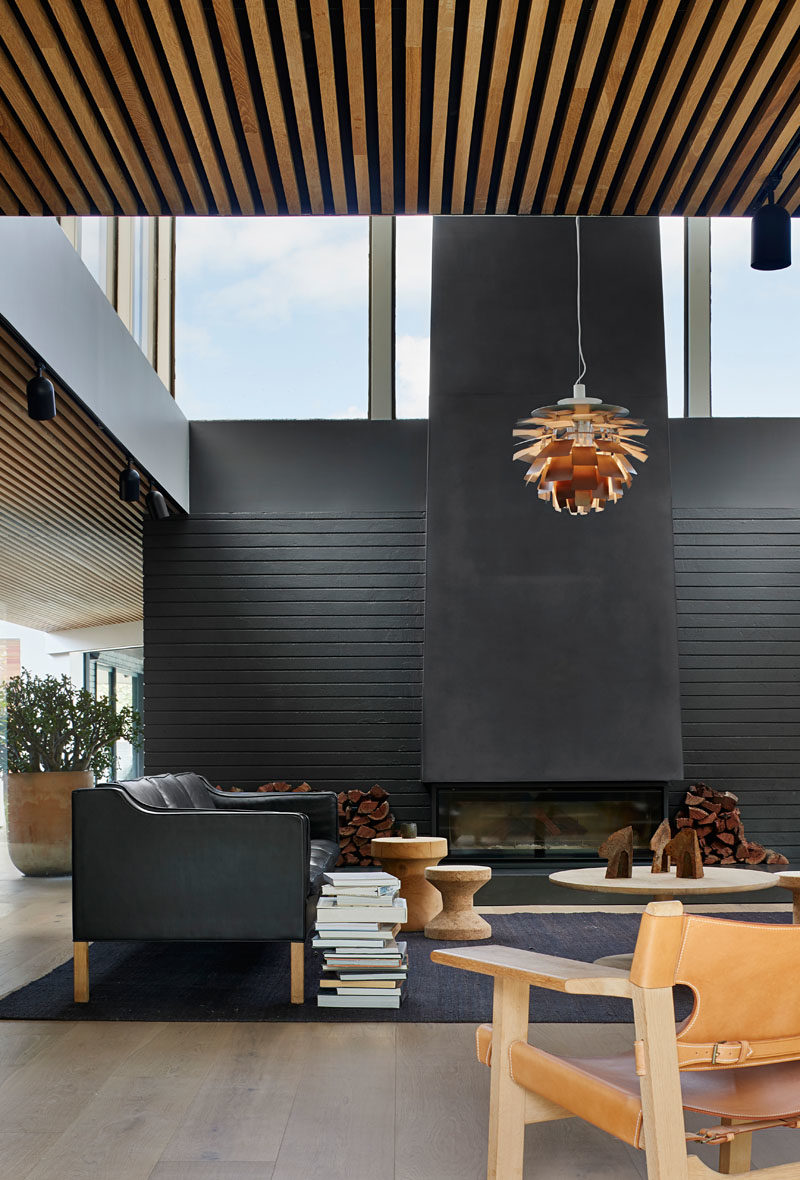 Living Room Ideas - In this modern living room, a large black steel fireplace commands attention, while a single pendant light anchors the rug and furniture in the open space. #ModernLivingRoom #LivingRoomIdeas #BlackLivingRoom #BlackFireplace