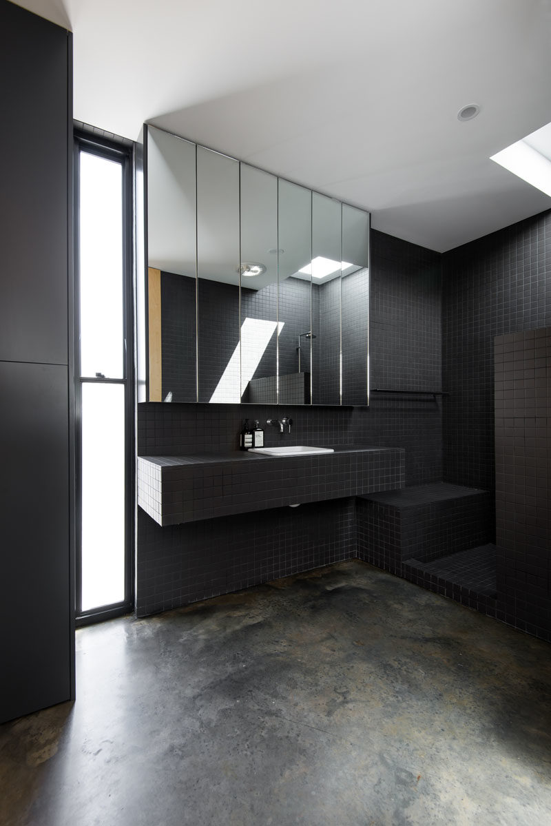 Bathroom Ideas - This modern bathroom features a fully tiled ensuite bathroom, that showcases small black tiles, an open shower with a skylight, a frosted window, and a mirror with hidden shelving. #BathroomIdeas #BlackBathroom #ModernBathroom