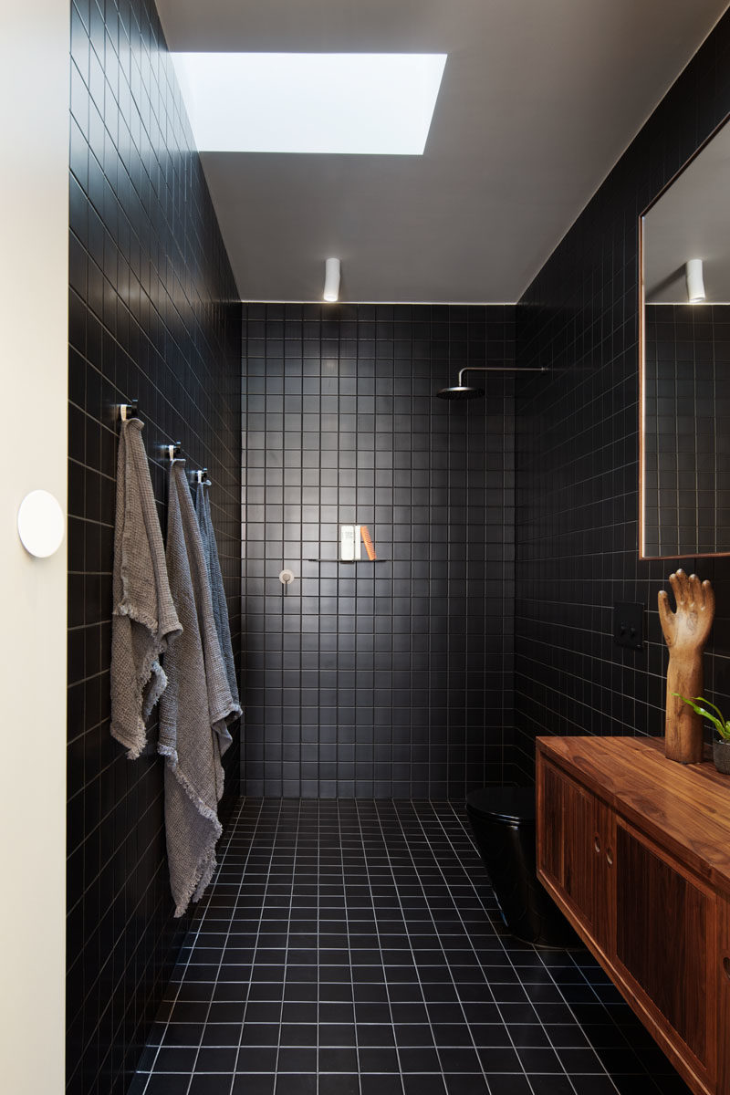 Black Bathroom - This modern bathroom features square black tiles that cover the walls and floor. A skylight helps to keep the room bright. #BathroomIdeas #BlackBathroom #ModernBathroom