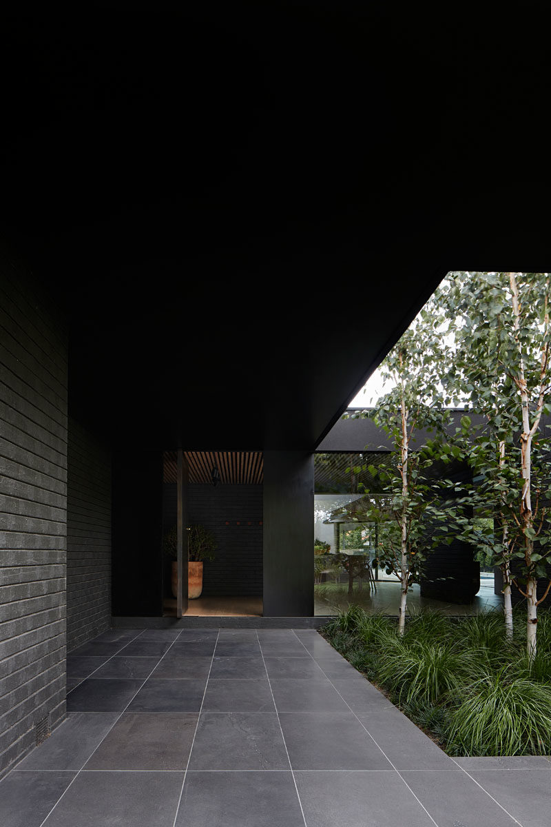 On arrival to this modern black house, the entry is defined by an oversized eave that's been punctured to allow soft landscaping adjacent the entrance, as well as provide increased light into the interior of the home. #ModernHouse #BlackHouse #HouseDesign #Landscaping