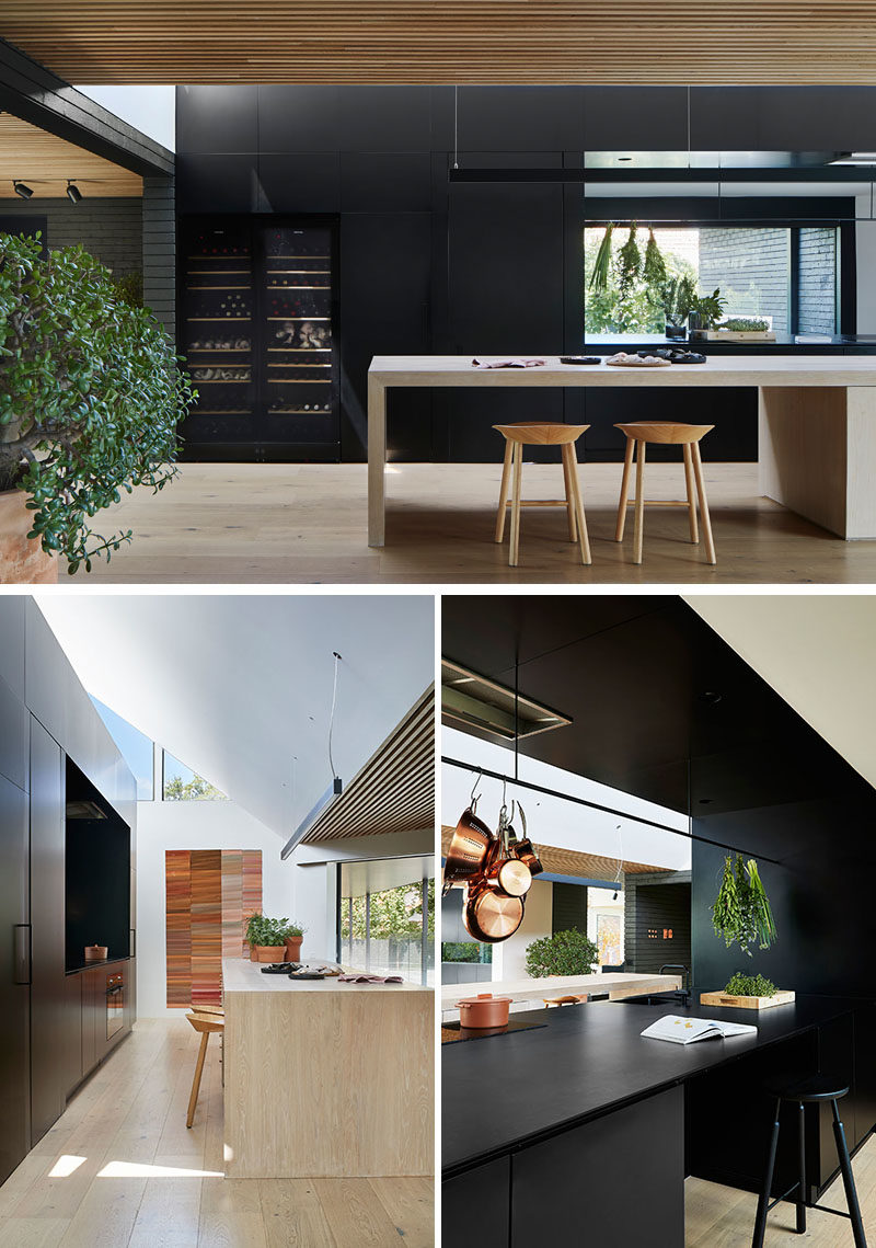 Kitchen Ideas - In this modern kitchen, minimalist black cabinets line the wall, and a large island provides ample counter space and a place for sitting. A void in the cabinets allows for connectivity between the kitchen and the pantry, that's located behind the cabinets. #KitchenIdeas #BlackKitchen #KitchenDesign #ModernKitchen