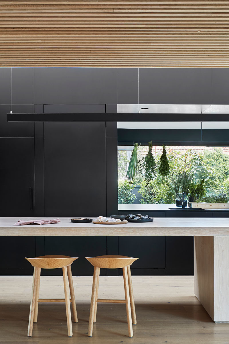 Kitchen Ideas - In this modern kitchen, minimalist black cabinets line the wall, and a large island provides ample counter space and a place for sitting. A void in the cabinets allows for connectivity between the kitchen and the pantry, that's located behind the cabinets. #KitchenIdeas #BlackKitchen #KitchenDesign #ModernKitchen