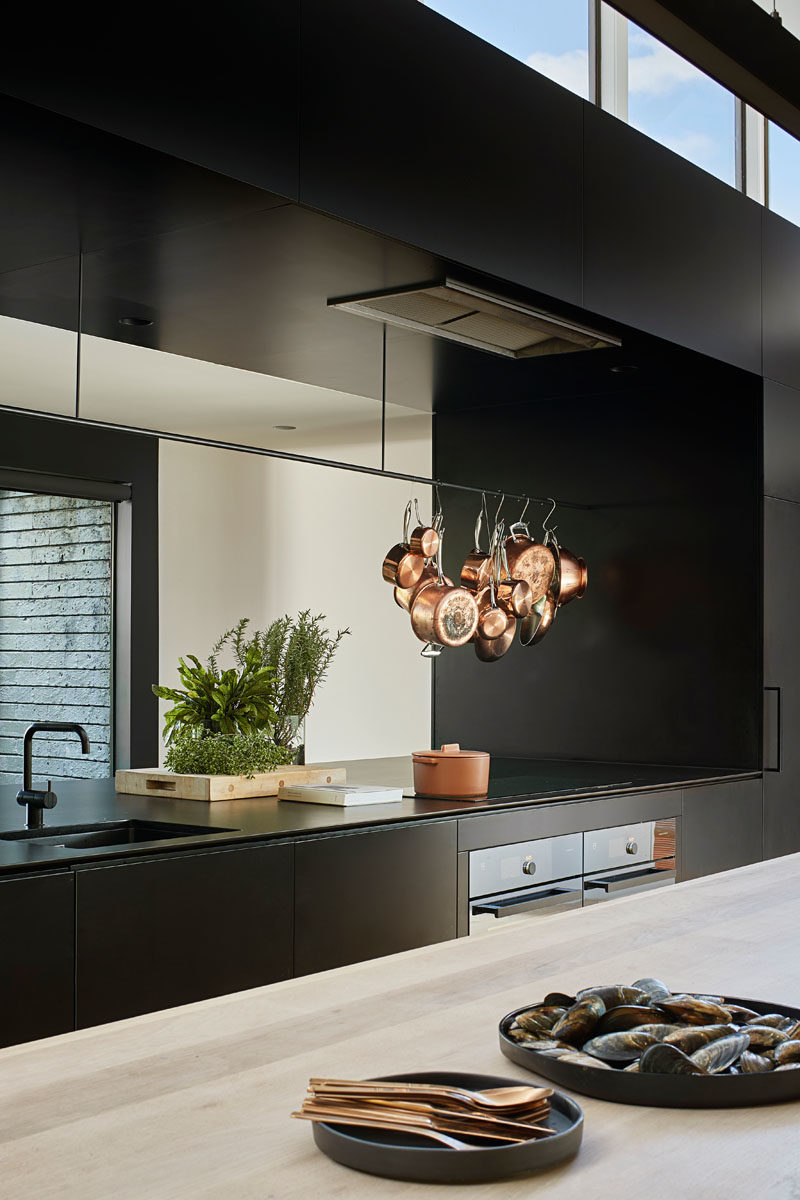 Kitchen Ideas - In this modern kitchen, minimalist black cabinets line the wall, and a large island provides ample counter space and a place for sitting. A void in the cabinets allows for connectivity between the kitchen and the pantry, that's located behind the cabinets. #KitchenIdeas #BlackKitchen #KitchenDesign #ModernKitchen