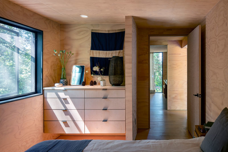 In this wood-lined bedroom, a picture window provides natural light and an uninterrupted view of the trees. #BedroomIdeas #BuiltInStorage #Windows #Bedroom