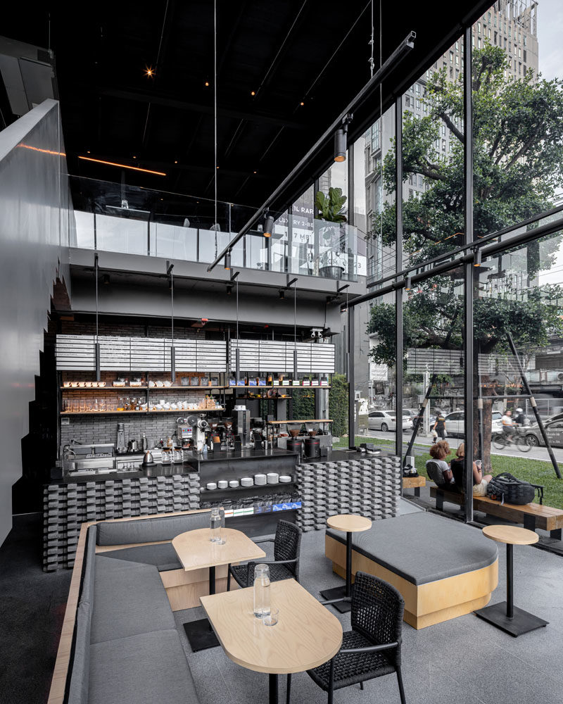 The main floor of this modern coffee shop is home to the service bar, where natural oak woods with rounded edges have been complemented by light grey cushions and banquettes. #CoffeeShop #ModernCafe #CoffeeShopDesign #InteriorDesign