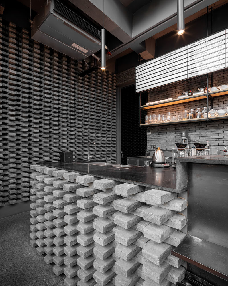 This modern coffee shop has a distinct grey brick pattern, that was installed at the counter bar and on the wall, adding a unique design element to the space. #GreyBricks #CoffeeShop #GreyBrick #InteriorDesign