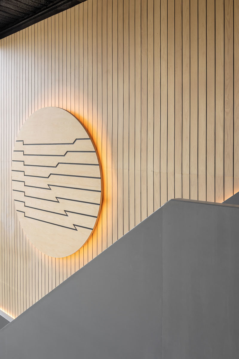 This modern coffee shop has a  tall wood-lined wall that's accented with a large wood disc, that also has a warm glow from the hidden lighting behind it. #CoffeeShopDesign #CoffeeShop #WoodWall