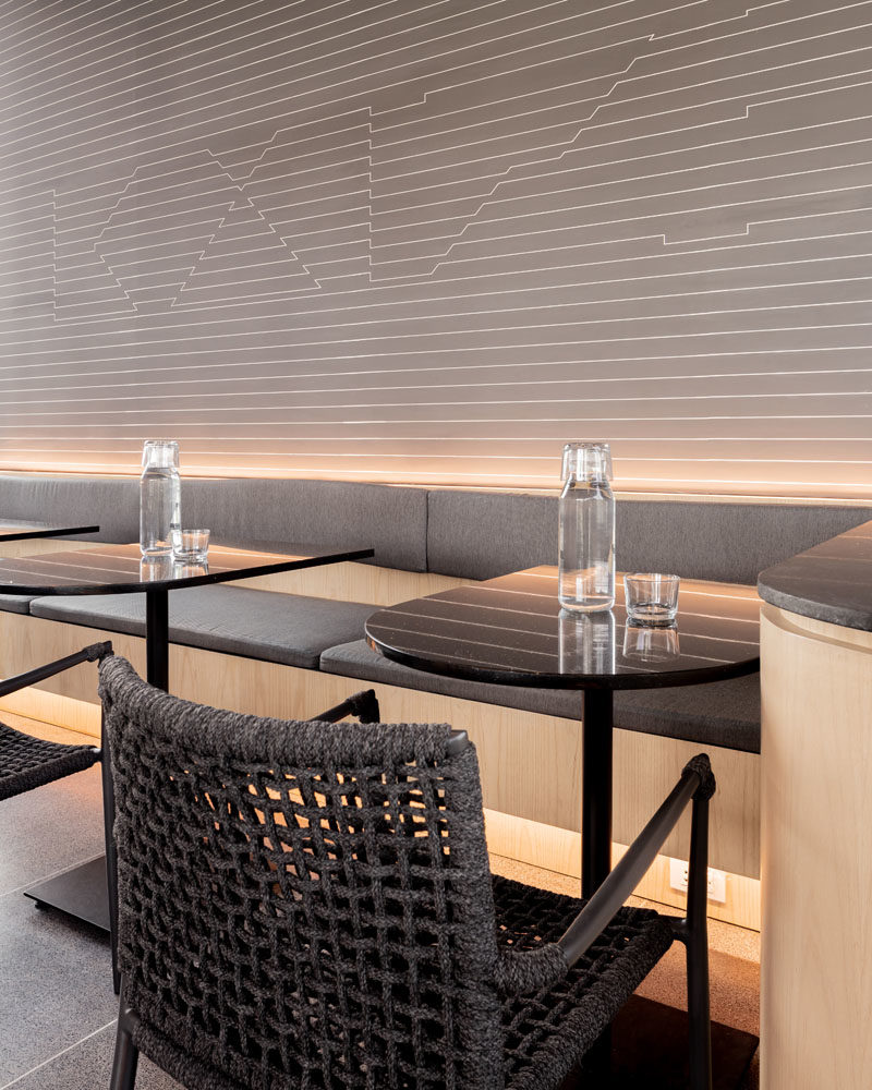 This modern coffee shop has hidden lighting underneath tables and behind the seating, creating a soft glow for the black, grey, and wood interior. #ModernCoffeeShop #CafeDesign #Lighting