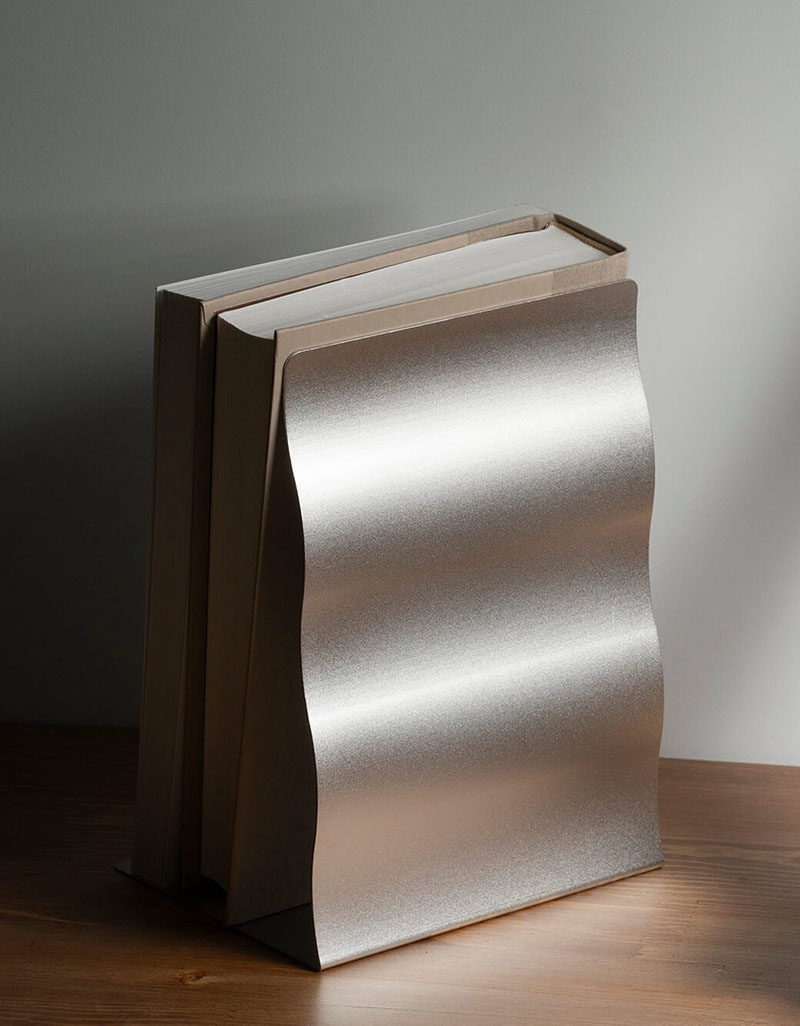 Gift Ideas - Named the 'Wave Stand', these modern bookends provide a steady support for different objects to lean on. Their design was inspired by the waves that occur in nature, with the stainless steel plate shaped to mimic the softness and the organic expression of nature. A sandblast finish has been applied to create a natural sparkling texture. #Bookends #ModernBookend #GiftIdea #ModernDecor #HomeOfficeAccessories #DeskAccessories
