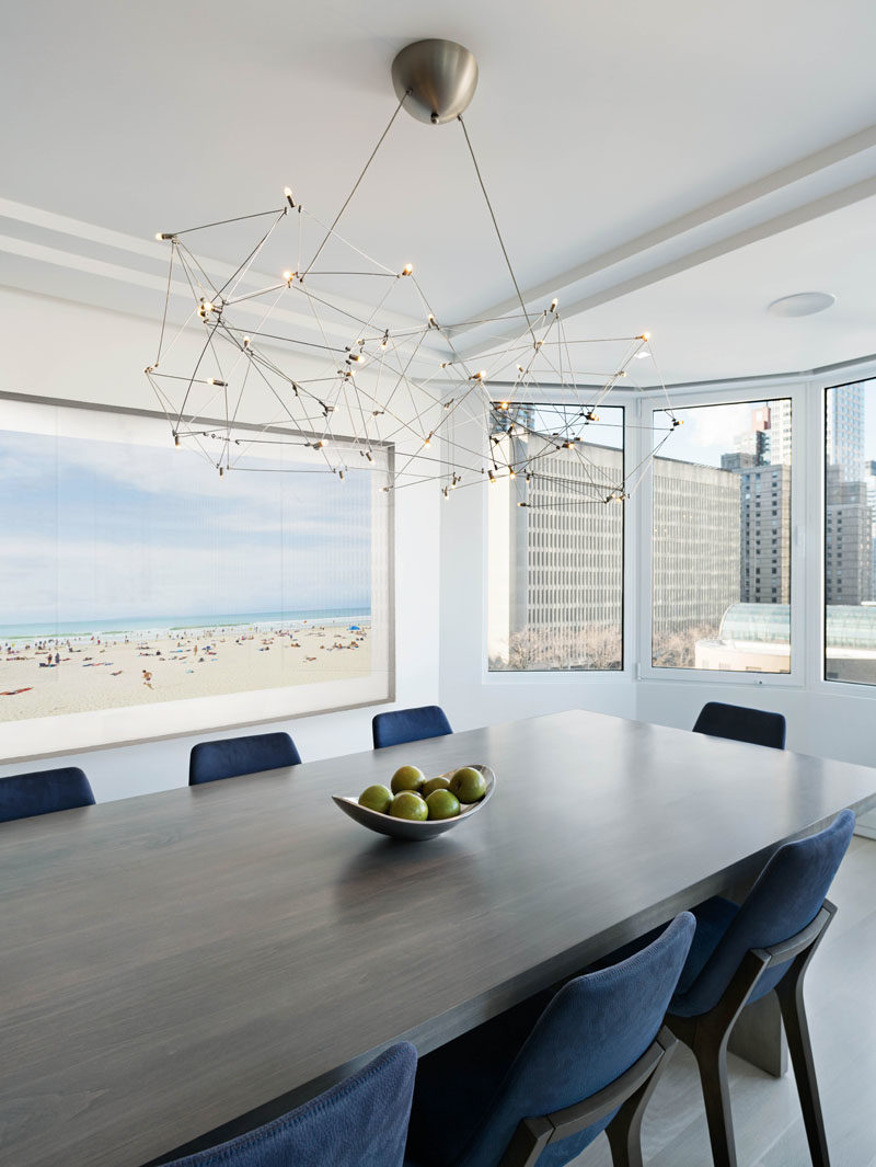 Dining Room Ideas - In this modern dining room, a curved section of windows provides views of the city, while a sculpture metal chandelier anchors the dining table in the space. #DiningRoomIdeas #ModernDiningRoom