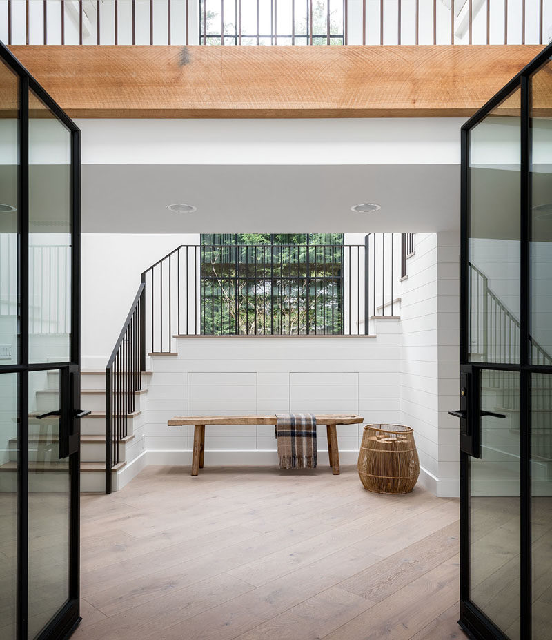 Black-framed glass doors welcome visitors to this modern farmhouse, where they'll find the entryway, and a view of an interior bridge.