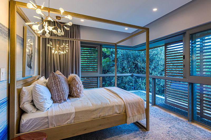 Bedroom Ideas - In this bedroom that features a modern four-poster bed, wood shutters provide privacy without blocking the surrounding tree views. #ModernBedroom #BedroomIdeas #WindowShutters #MasterBedroom