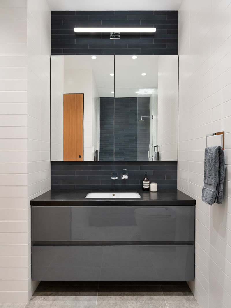 Bathroom Ideas - This modern bathroom features a glossy grey lacquer vanity, while dark skinny tiles laid horizontally contrast the white subway tiles. #BathroomIdeas #BathroomVanity #VanityIdeas #GreyCabinets #ModernBathroom