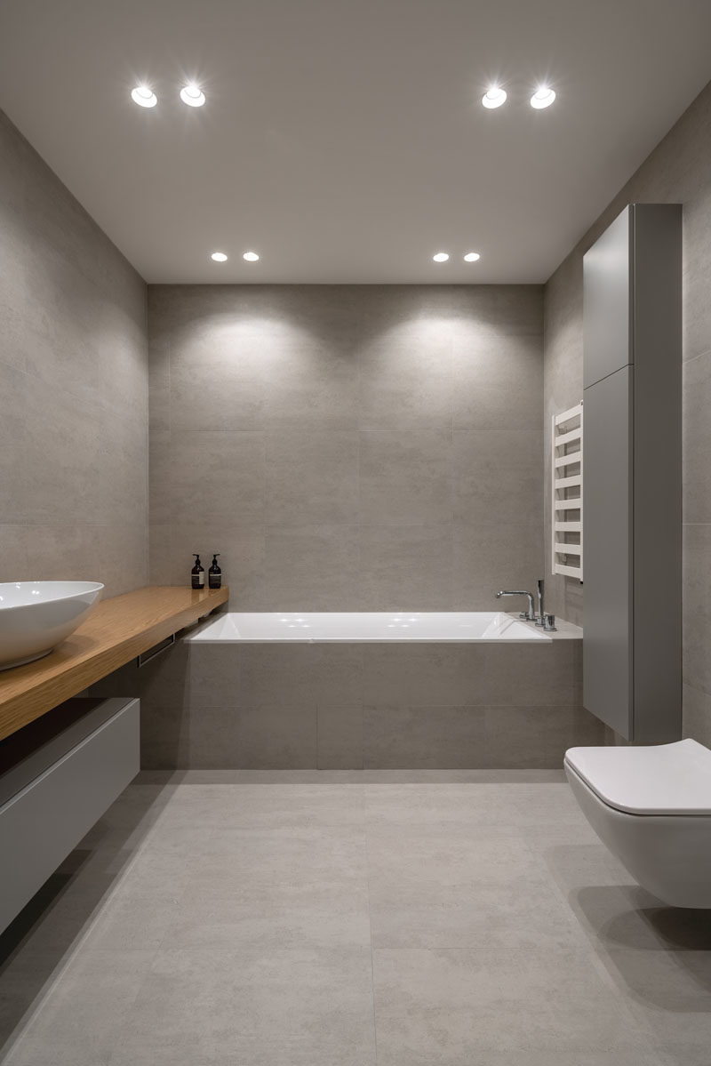 Bathroom Ideas - In this modern bathroom, large format grey tiles cover the walls and floor, while the wood vanity adds a natural touch. #ModernBathroom #BathroomDesign #BathroomIdeas