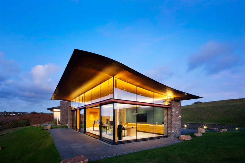 The design of this modern house includes a wave-like roofs that appears to 'float' above the walls of glass, while the stone work complements the surroundings and the traditional of dry stone walling found in Jersey. #ModernArchitecture #HouseDesign #GlassWalls #WavyRoof