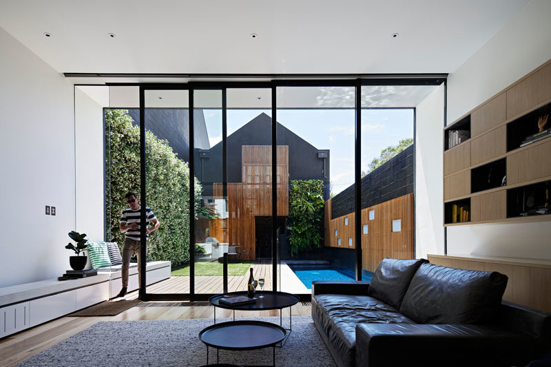 This modern house has sliding glass doors that open the living room to the outdoor space, that features a patio, yard, green wall, and swimming pool. #GlassWall #SwimmingPool #LandscapeDesign