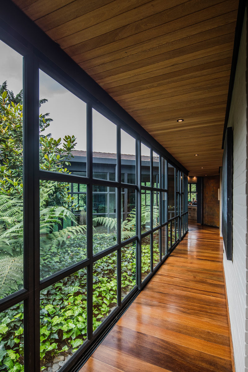 A central open-air garden filled with plants connects the wings of this modern house, with sliding glass walls opening the garden to the interior. #Garden #ModernHouse #Architecture #InteriorGarden #Landscaping #GlassWalls