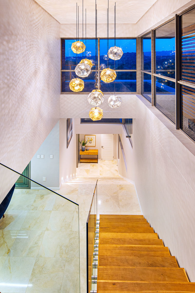 Stair Ideas - This modern house has wood stairs with glass handrails that connect the various floors of the home, while a collection of metallic pendant lights have added to fill the space with light. #StairIdeas #LightingIdeas #ModernStairs