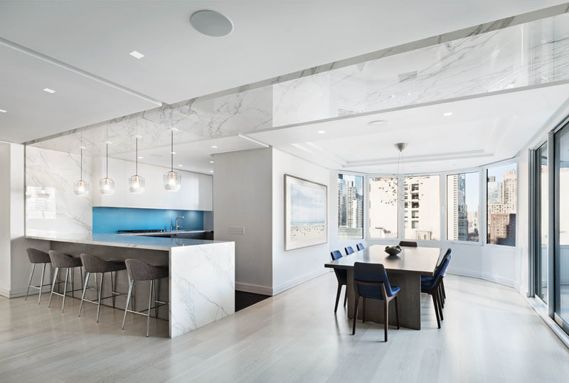 Kitchen Ideas - A bright blue backsplash in the kitchen adds a pop of color, while the marble counters extend up the wall and onto the ceiling marking the separation of the kitchen/dining area from the living room. #KitchenDesign #KitchenIdeas #ModernWhiteKitchen #WhiteKitchen #ModernKitchen