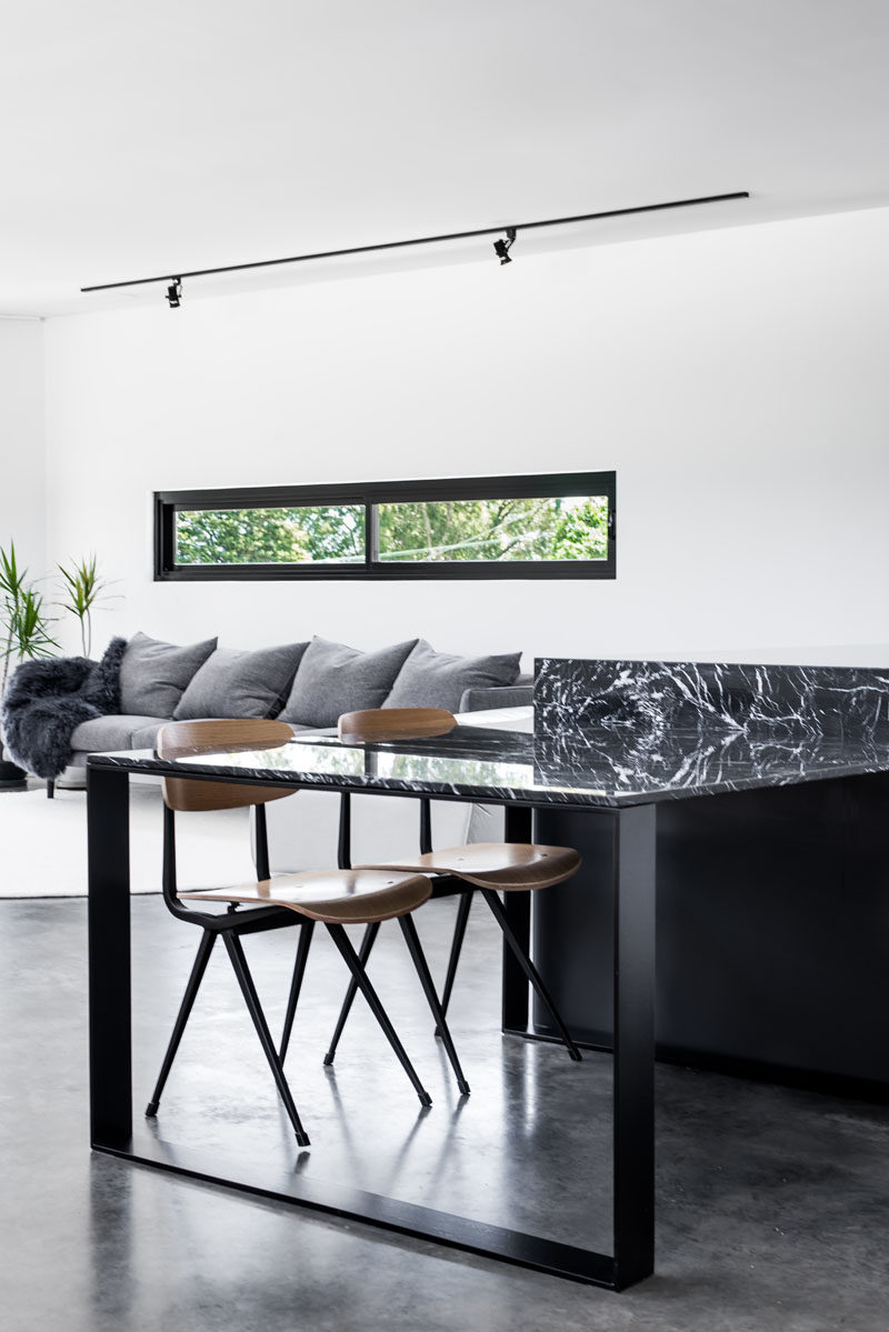Kitchen Ideas - Minimalist black and white cabinetry has been used in the kitchen, while the kitchen table is able to be moved when required. Marble bench tops complement the black powder coated steel and concrete floors. #ModernKitchen #KitchenIdeas #KitchenDesign