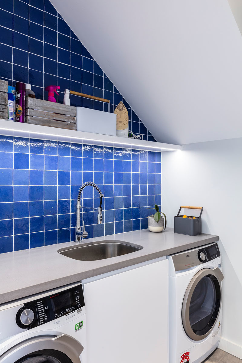 Laundry Room Ideas - This modern laundry room has a counter that runs across both the washing machine and dryer, while square blue tiles add some color and and upper shelf provides storage. #LaundryRoom #LaundryIdeas