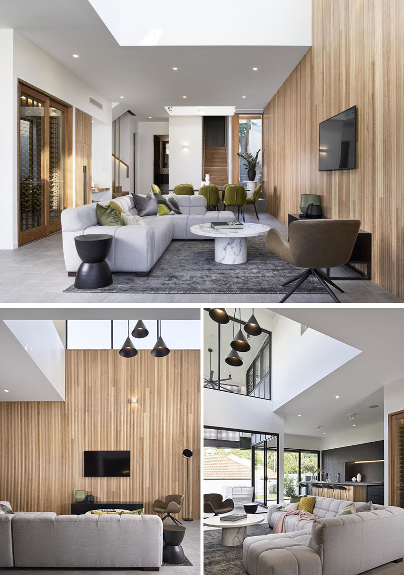 Living Room Ideas - A wood accent wall connects the dining area and living room in this modern house. A void above the living room is filled with multiple pendant lights, while a skylight adds natural light during the day. #LivingRoomIdeas #ModernLivingRoom #WoodAccentWall